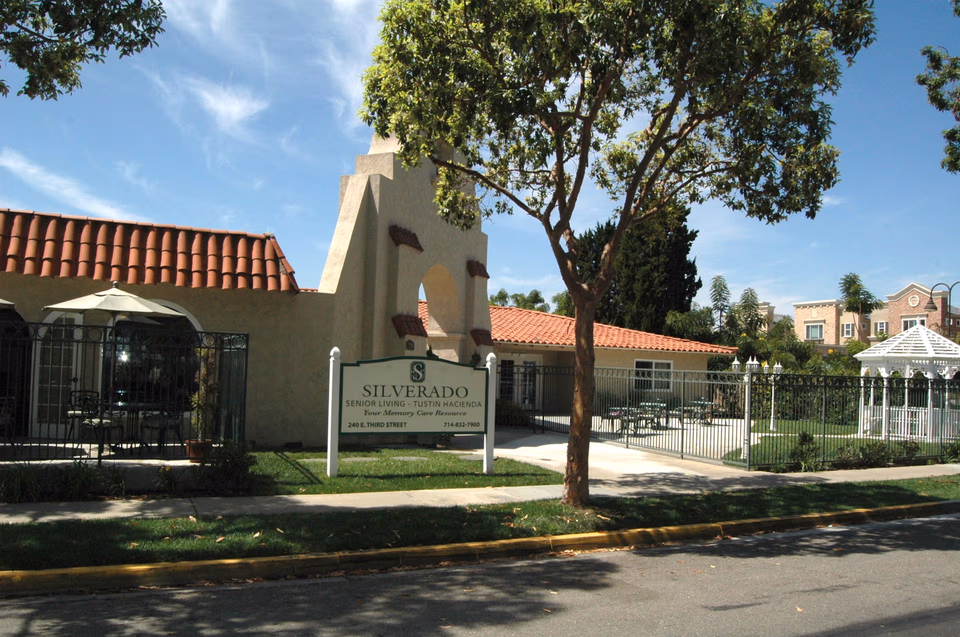 Exterior view of Silverado Tustin Hacienda Memory Care Community with sign, fence, and gated entrance.