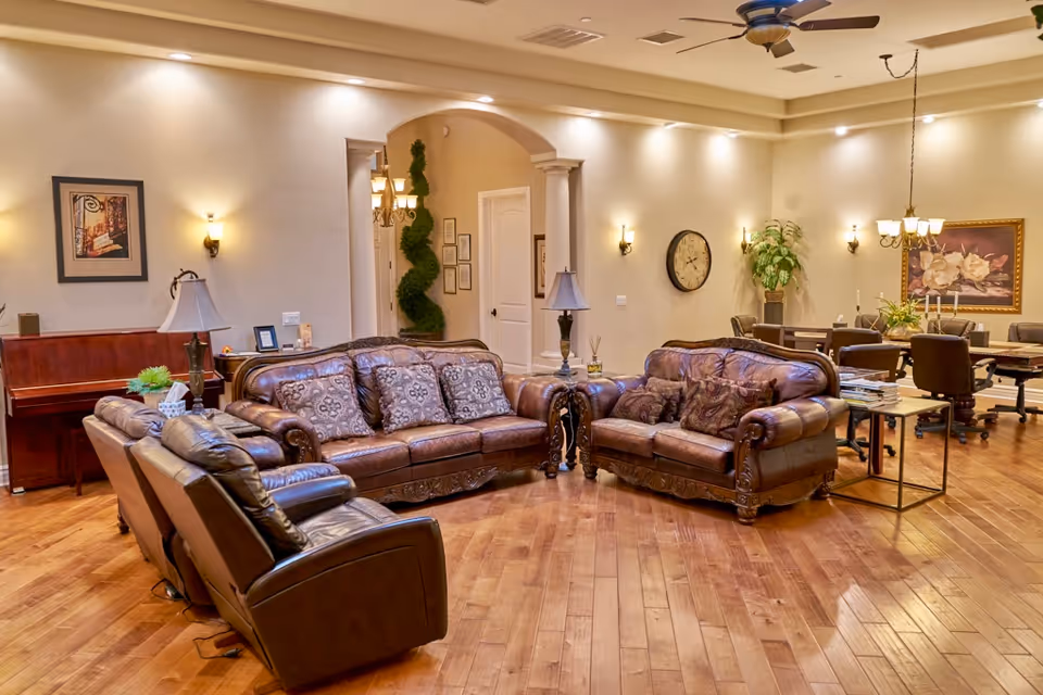 Spacious senior living lounge with leather sofas, lamps, and wood floors.