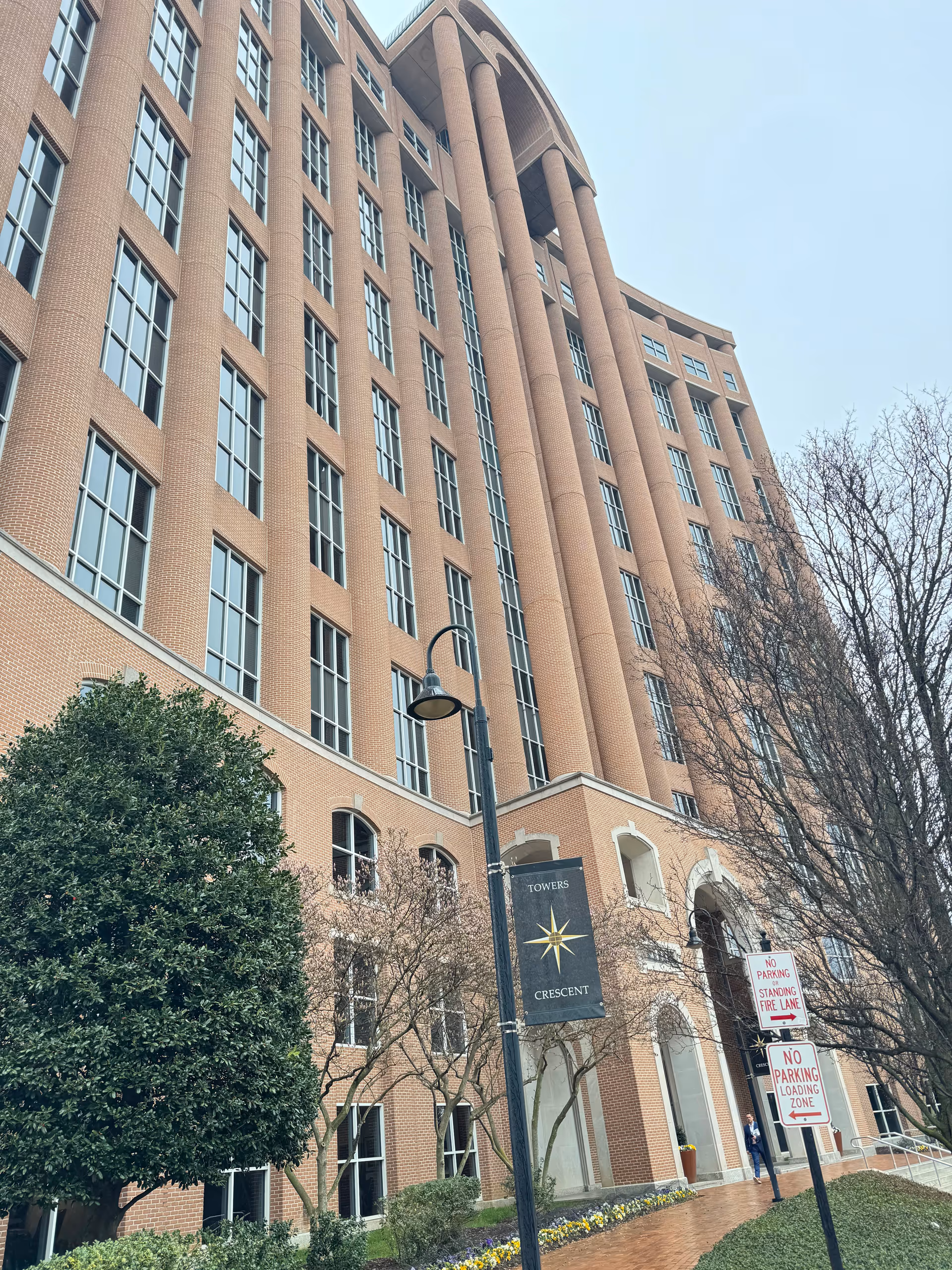 Tall brick senior living building exterior with arched entrance and trees.