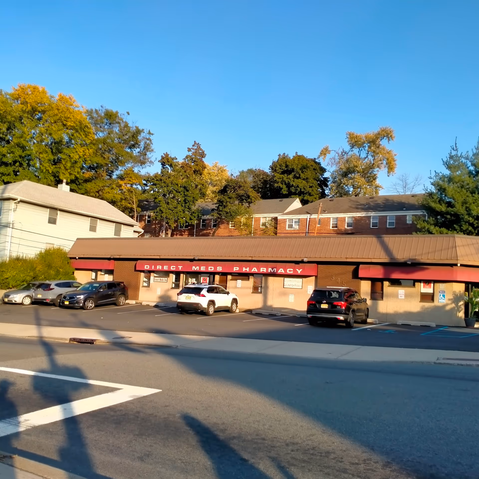 Front view of a storefront strip with Direct Meds Pharmacy and parked cars.
