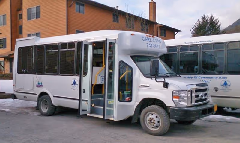 White shuttle bus parked outside a brick building with open doors