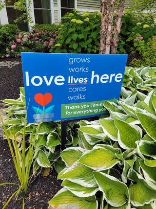 Blue sign with heart graphic among lush green plants outside Coastal Care Solutions.