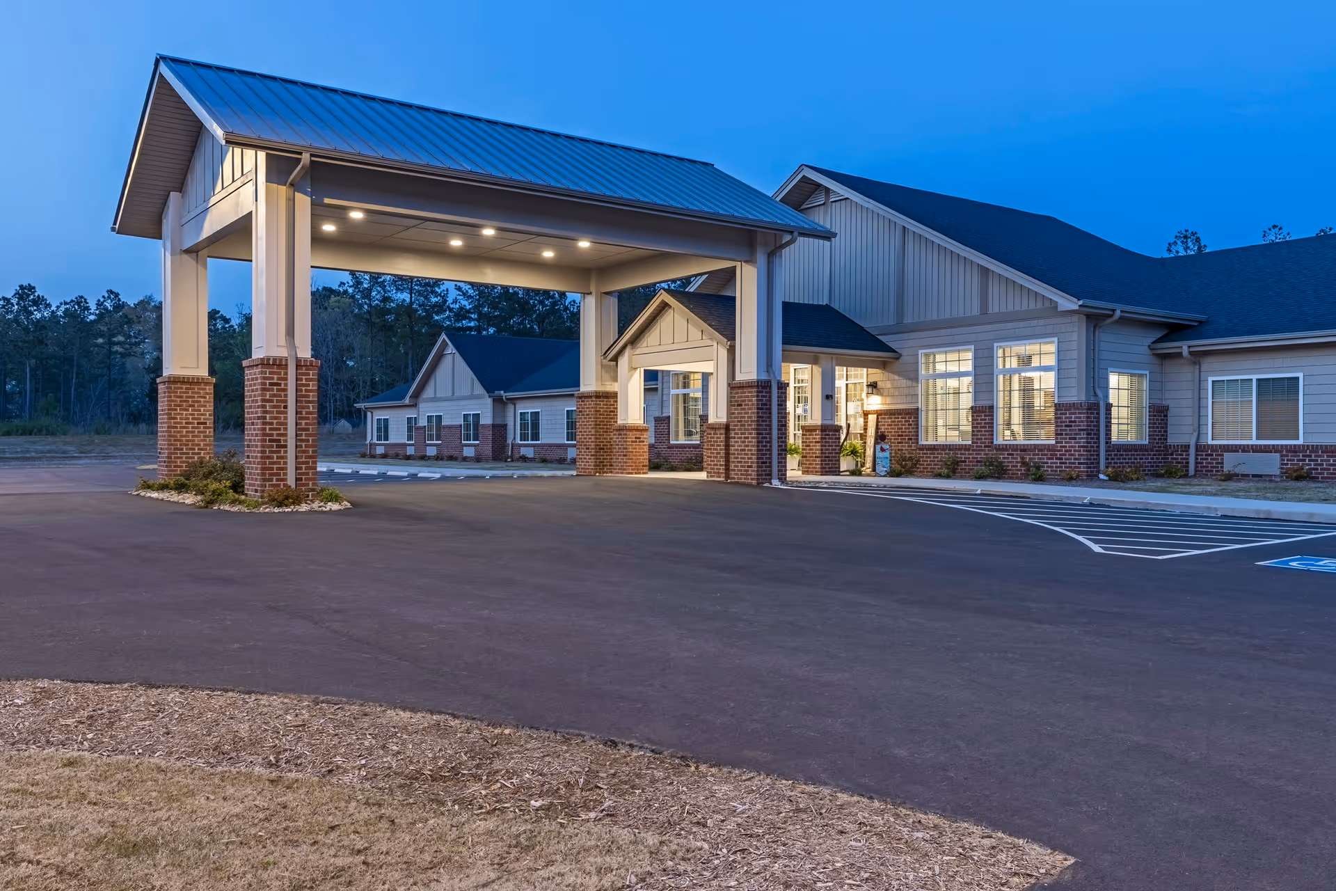 A senior living facility exterior with a covered entrance and well-lit front parking area.