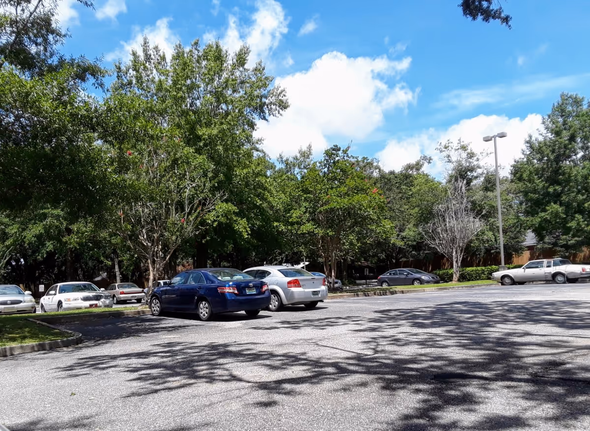 Parking lot with several cars and lush trees in front of a senior apartment complex.