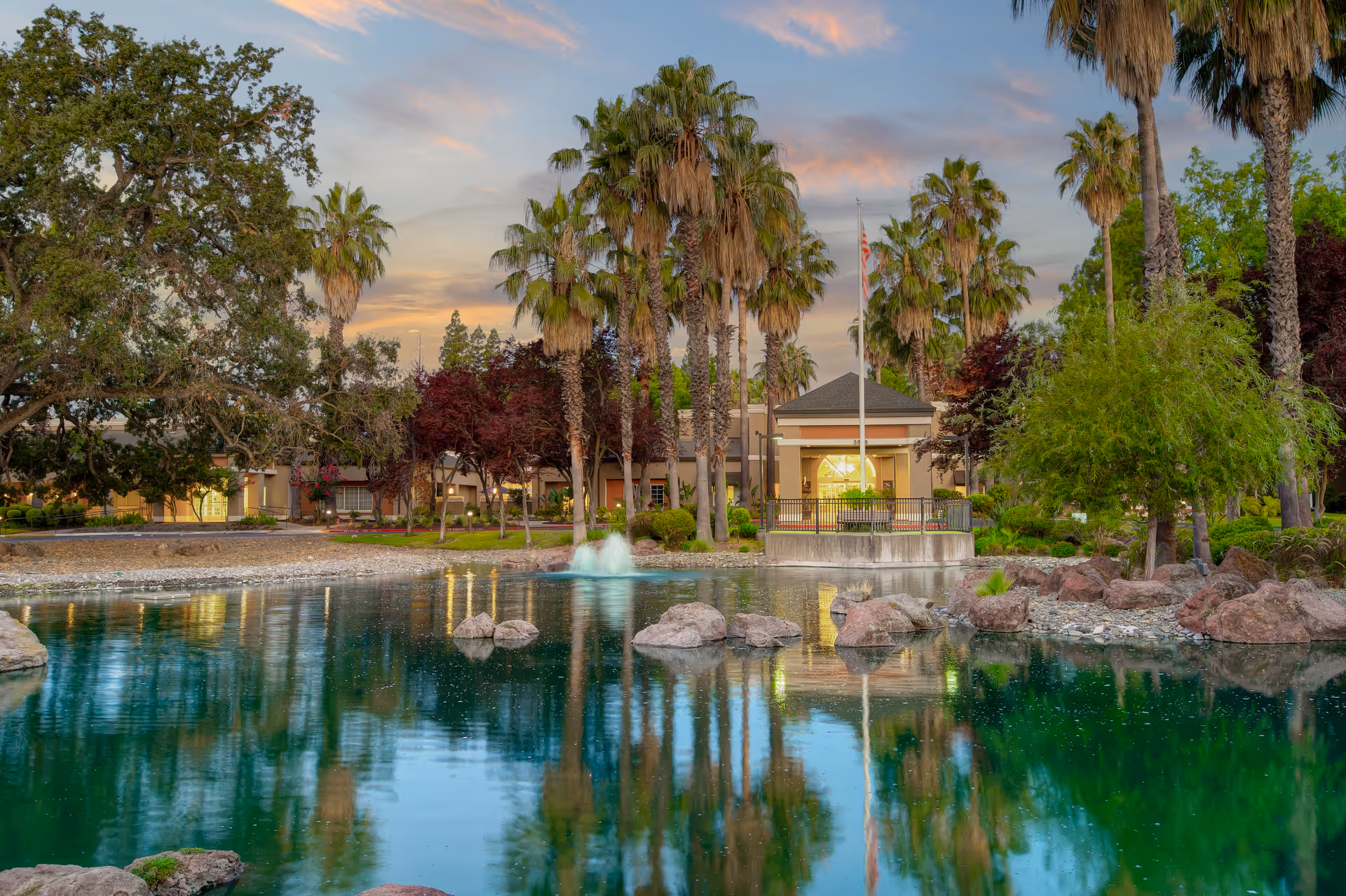 Sunlit outdoor view of Eskaton Village Carmichael with a pond, fountain, and palm trees.