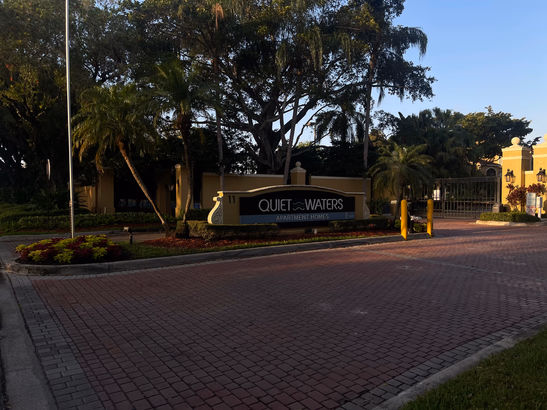 Entrance sign for Quiet Waters Apartment Homes with gate and palm trees.
