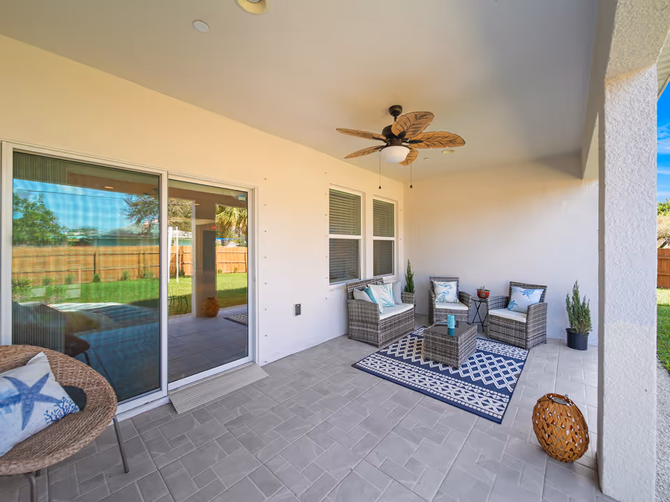 Covered outdoor patio with wicker seating, rug, and ceiling fan beside sliding doors.