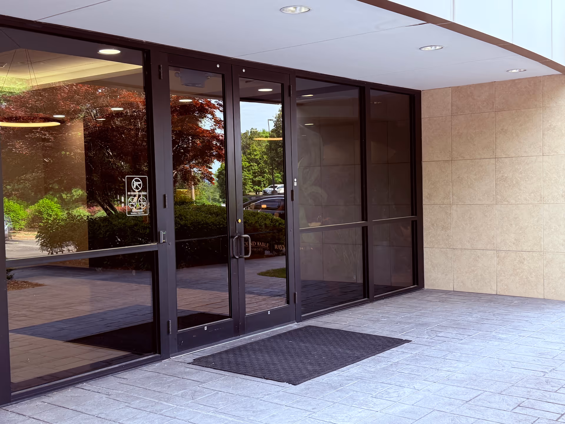 Glass doors of a modern building entrance with tiled walls and a mat.