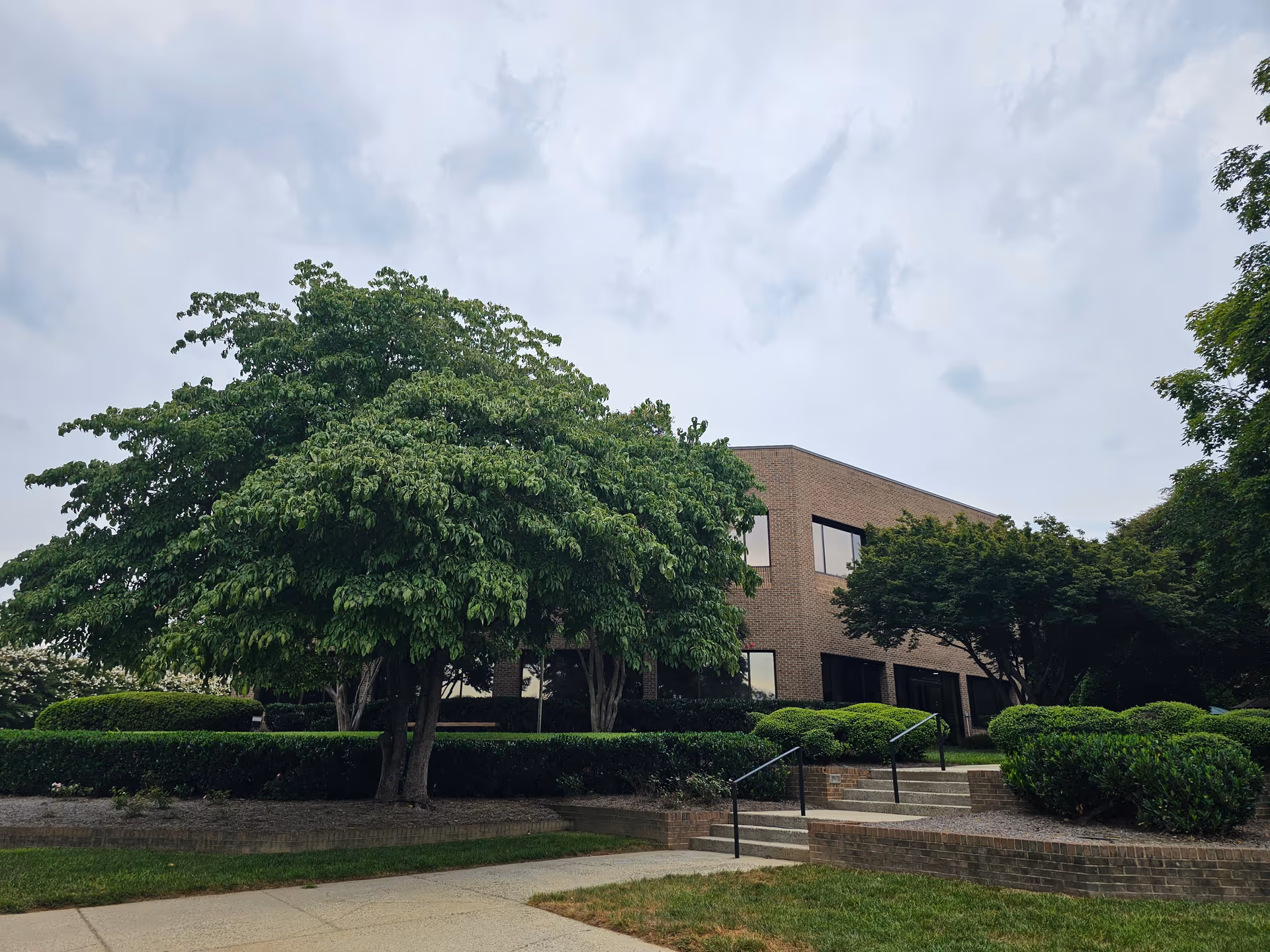 Brick exterior of a senior living building with trimmed trees and shrubs along a landscaped walkway.