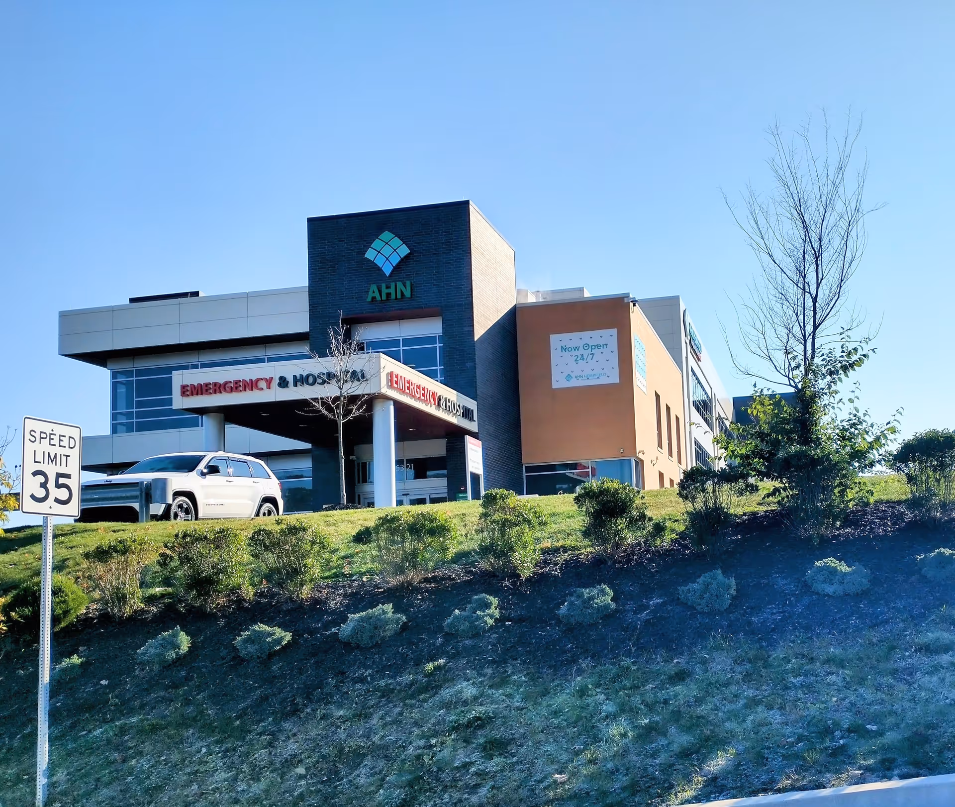 Modern hospital exterior with AHN logo, emergency entrance, and parking lot.