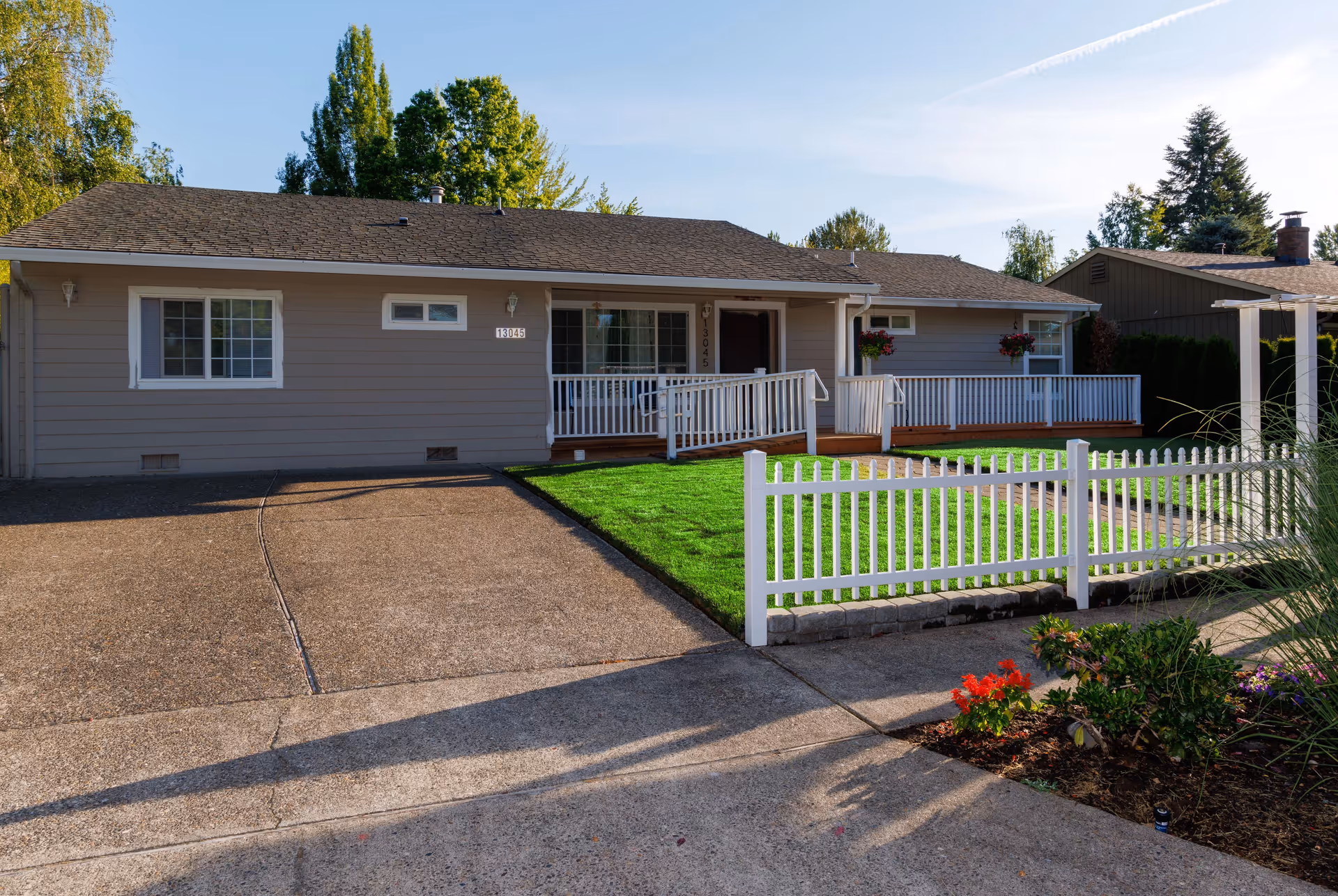 Front exterior of a single-story care home with a green lawn and white picket fence.