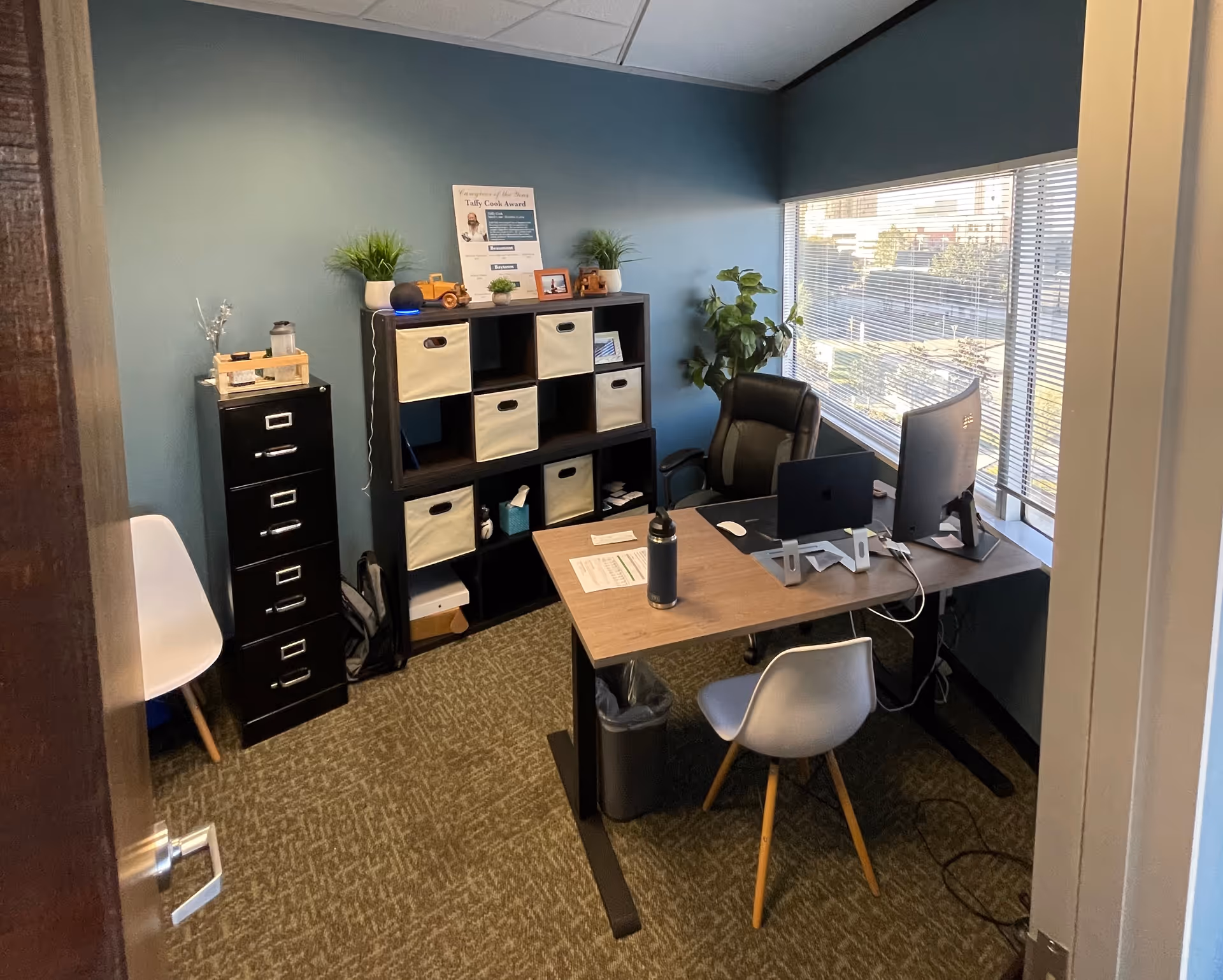 Small office with desk, computer, cubby storage, filing cabinet, and large window.