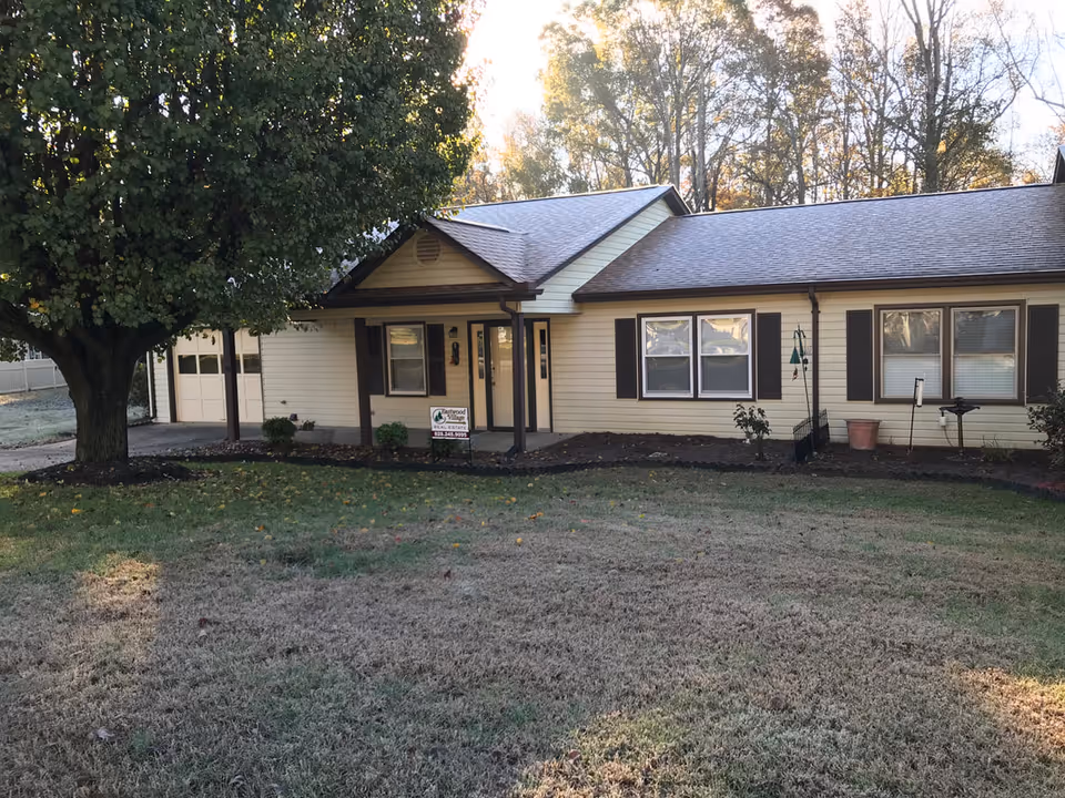 Single-story beige senior living home with front yard, large tree, and entrance.