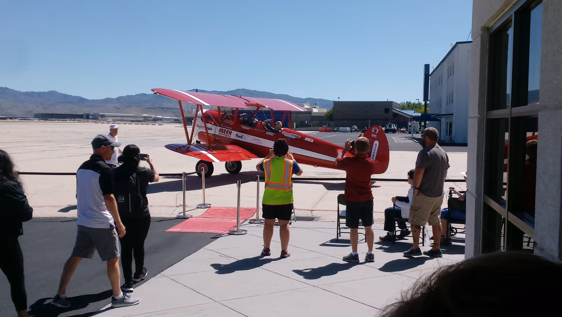 Red vintage airplane on a tarmac with several people watching outdoors.