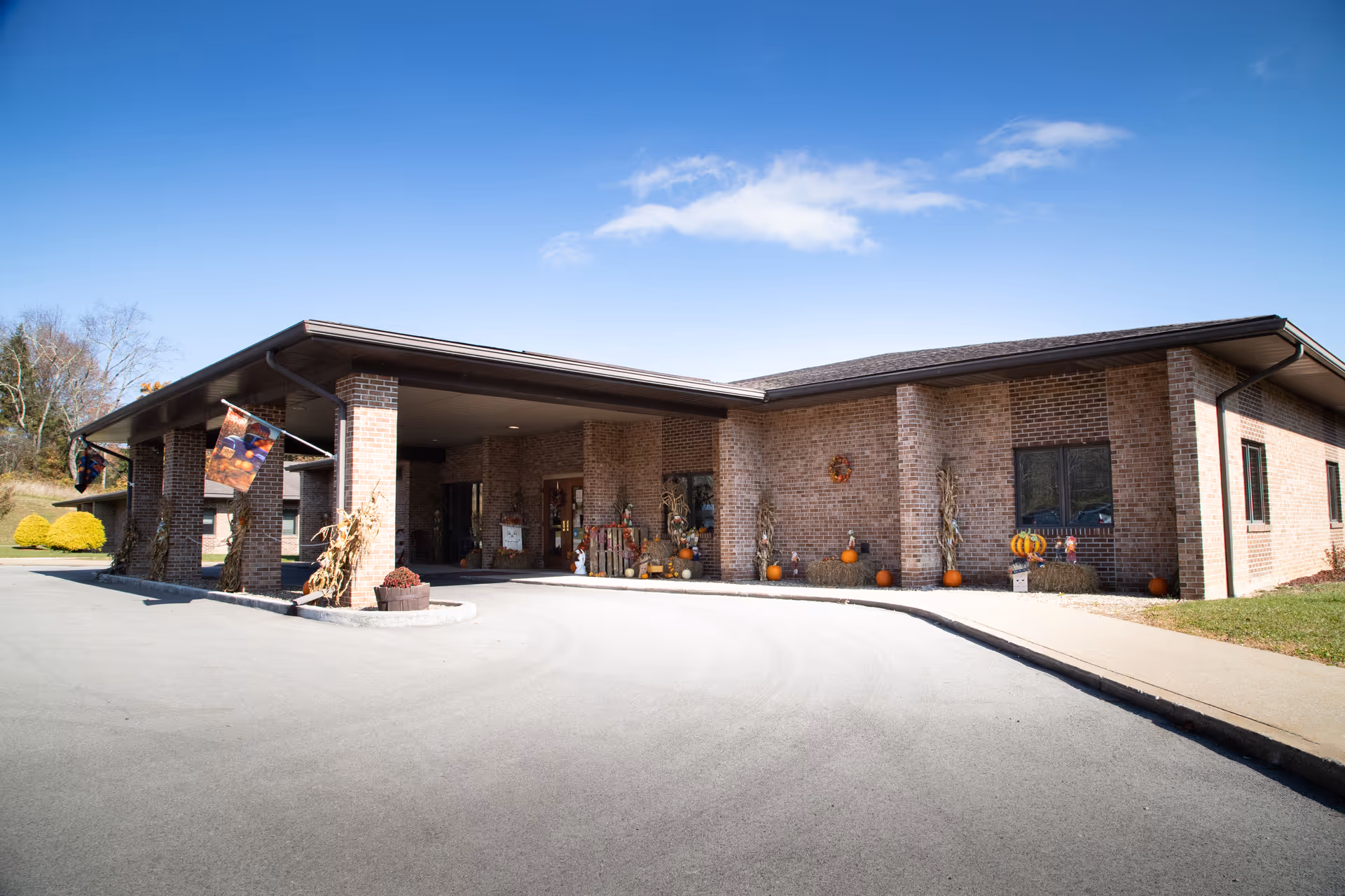 Exterior view of Autumn Lake Healthcare at Crystal Springs, brick building with curved driveway and pumpkins.