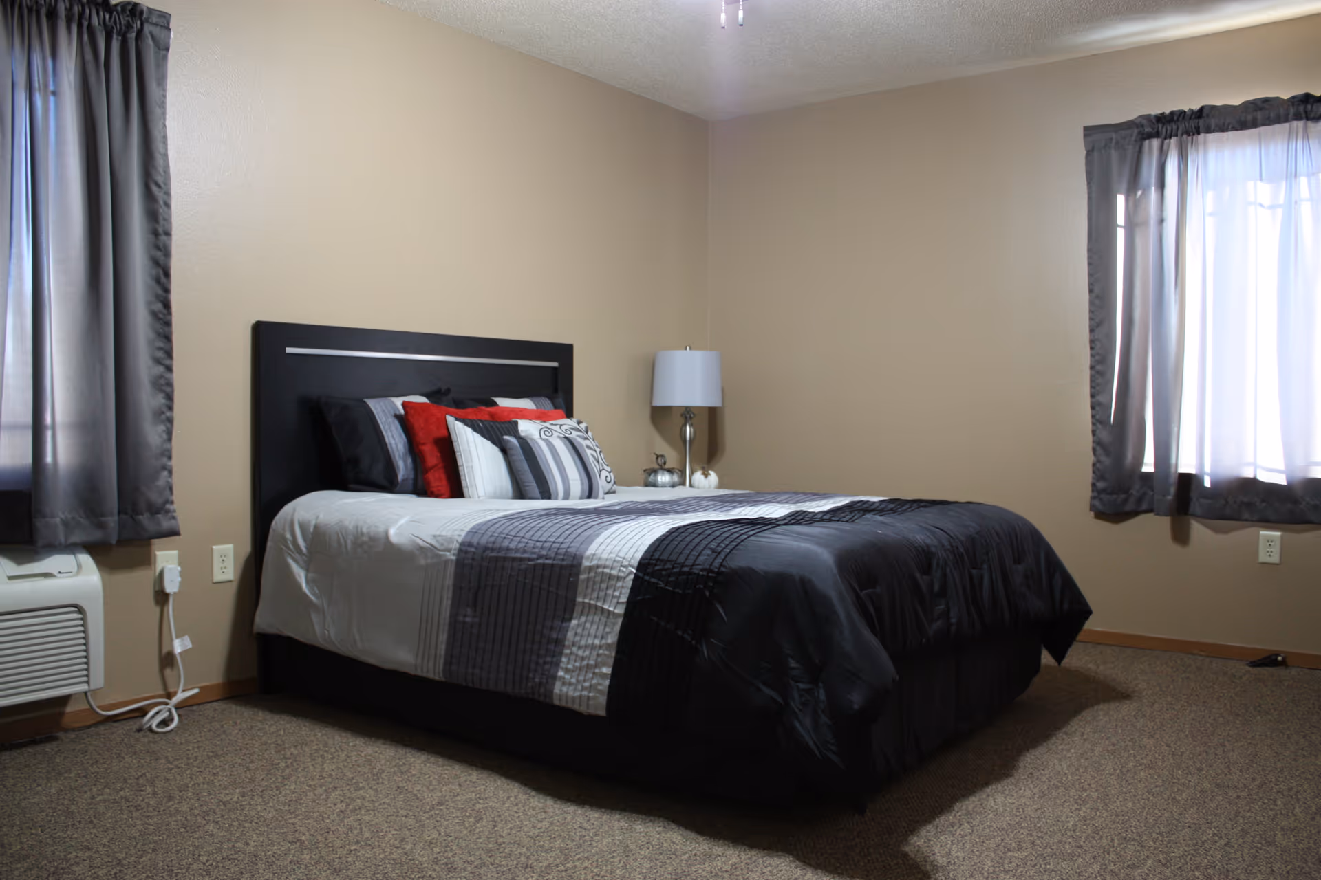 A neatly made bedroom with a dark headboard, striped bedding, and two windows.