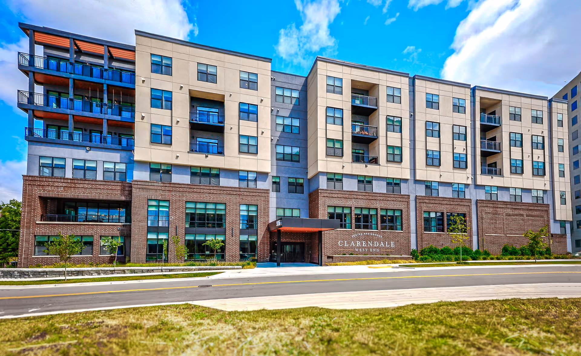 Exterior view of Clarendale West End senior living building with brick base and tan upper levels.