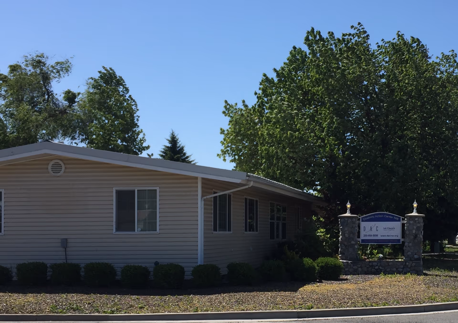 Beige single-story building with a front stone sign and shrubs.