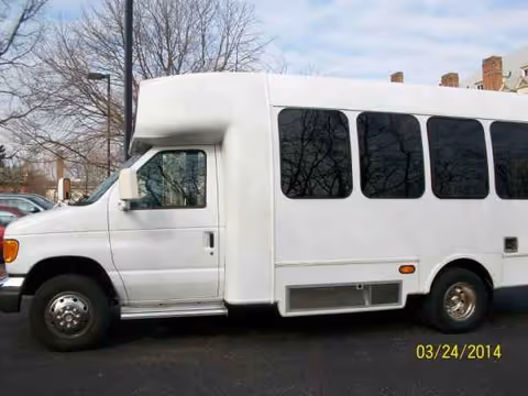 White shuttle bus parked on pavement with leafless trees in background