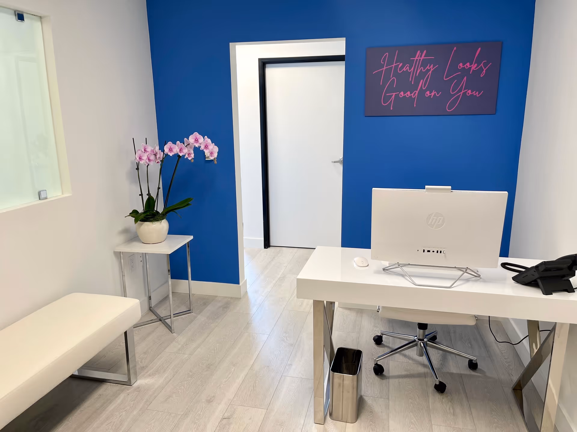 Bright modern reception area with blue accent wall, desk, computer, and orchid on side table.