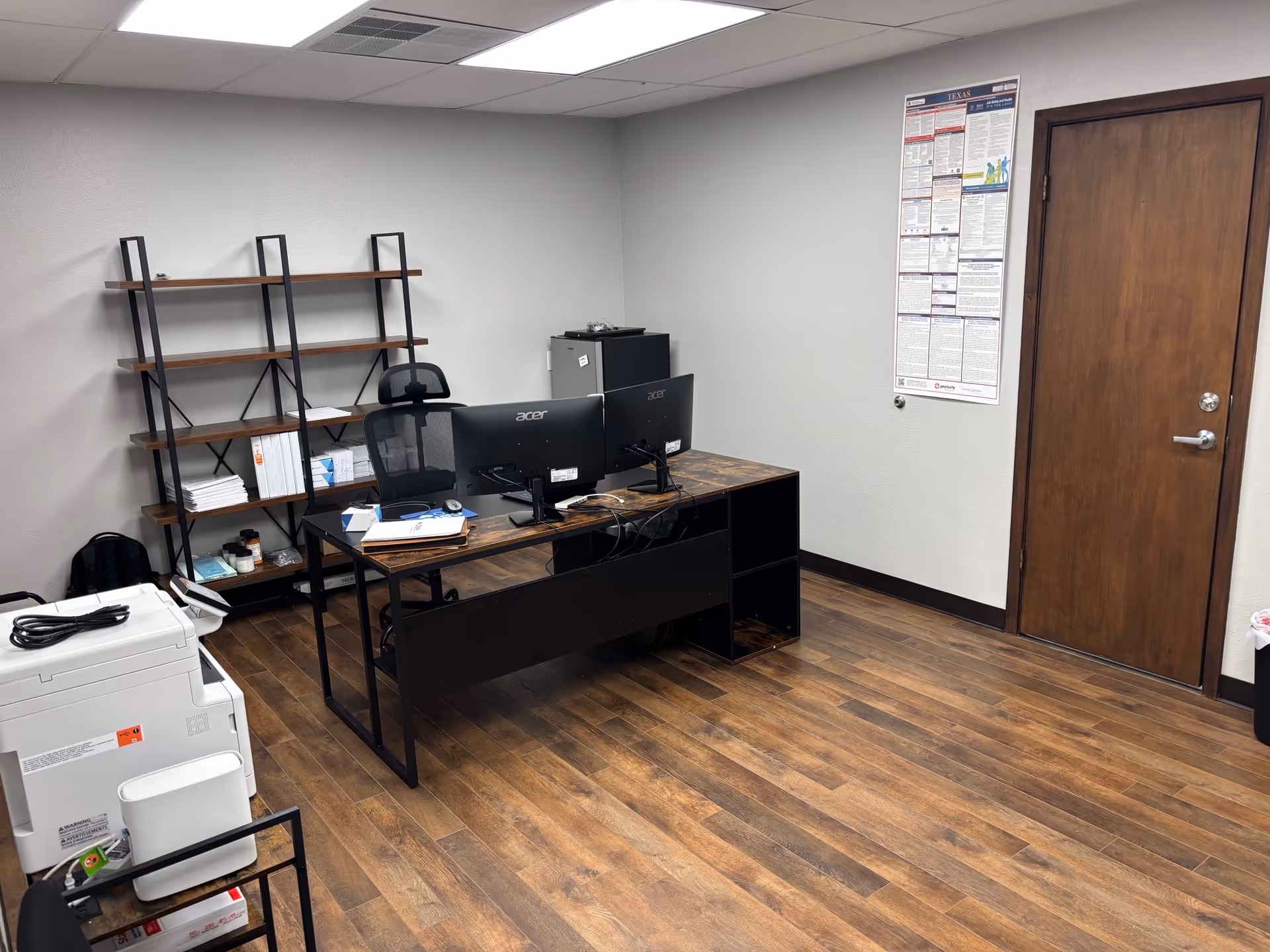 Office workspace with dual monitors, printer, and shelves in a senior care facility.