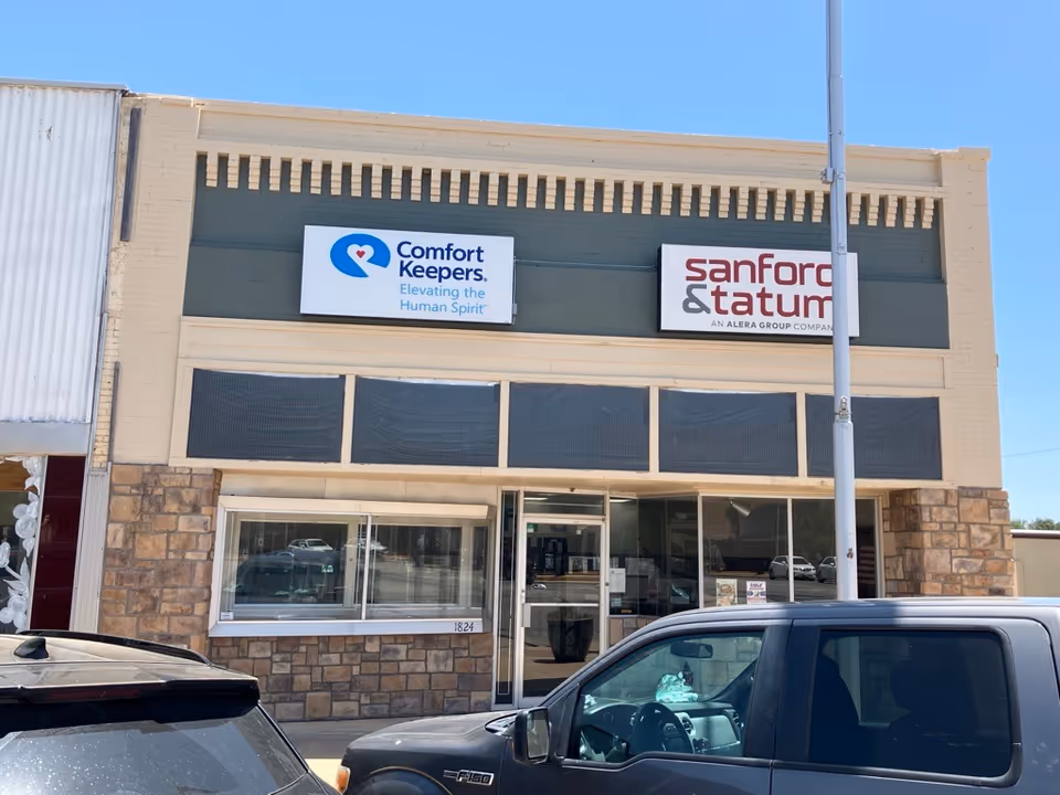 Storefront building with Comfort Keepers, Sanford & Tatum signage, stone facade, glass doors, parked cars.