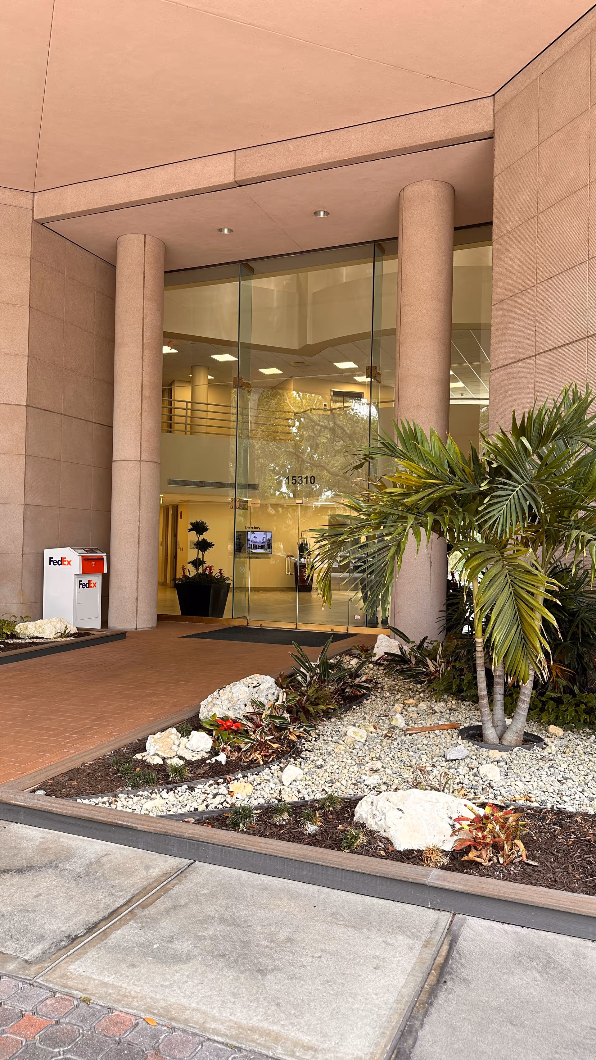 Exterior building entrance with glass doors, columns, and a landscaped front.