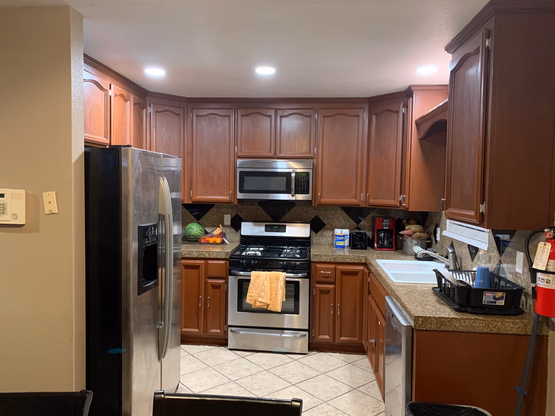 A kitchen with wooden cabinets, stainless appliances, a sink, and a dish rack.