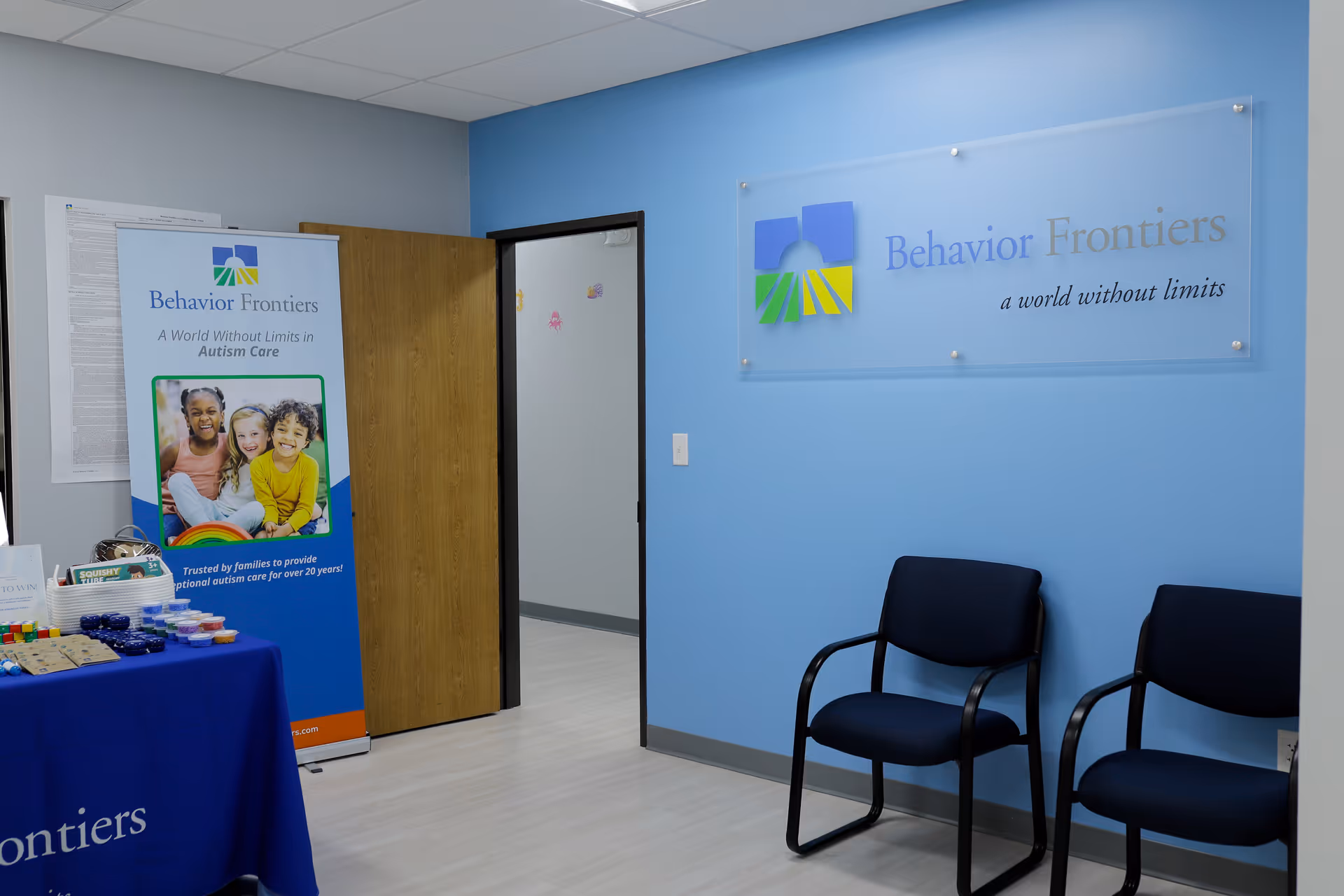 Reception area with blue walls, chairs, and a Behavior Frontiers sign beside a doorway.