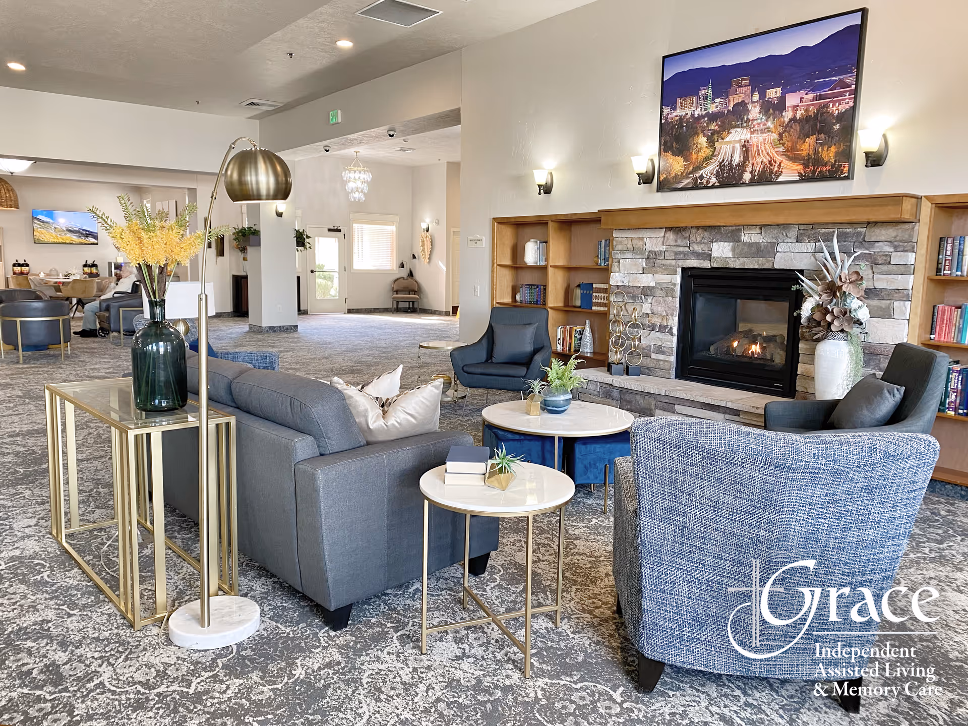 Spacious assisted living lounge with seating, a stone fireplace, and built-in bookshelves.