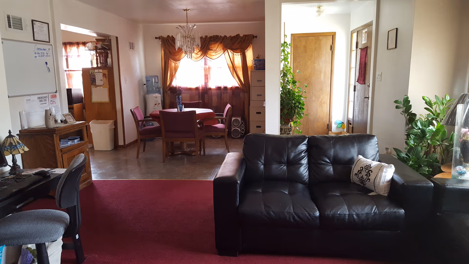 Cozy common living room with black leather sofa, red carpet, and dining area in back.