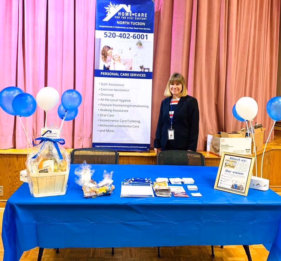 A woman stands behind a blue-covered booth table indoors with a banner.