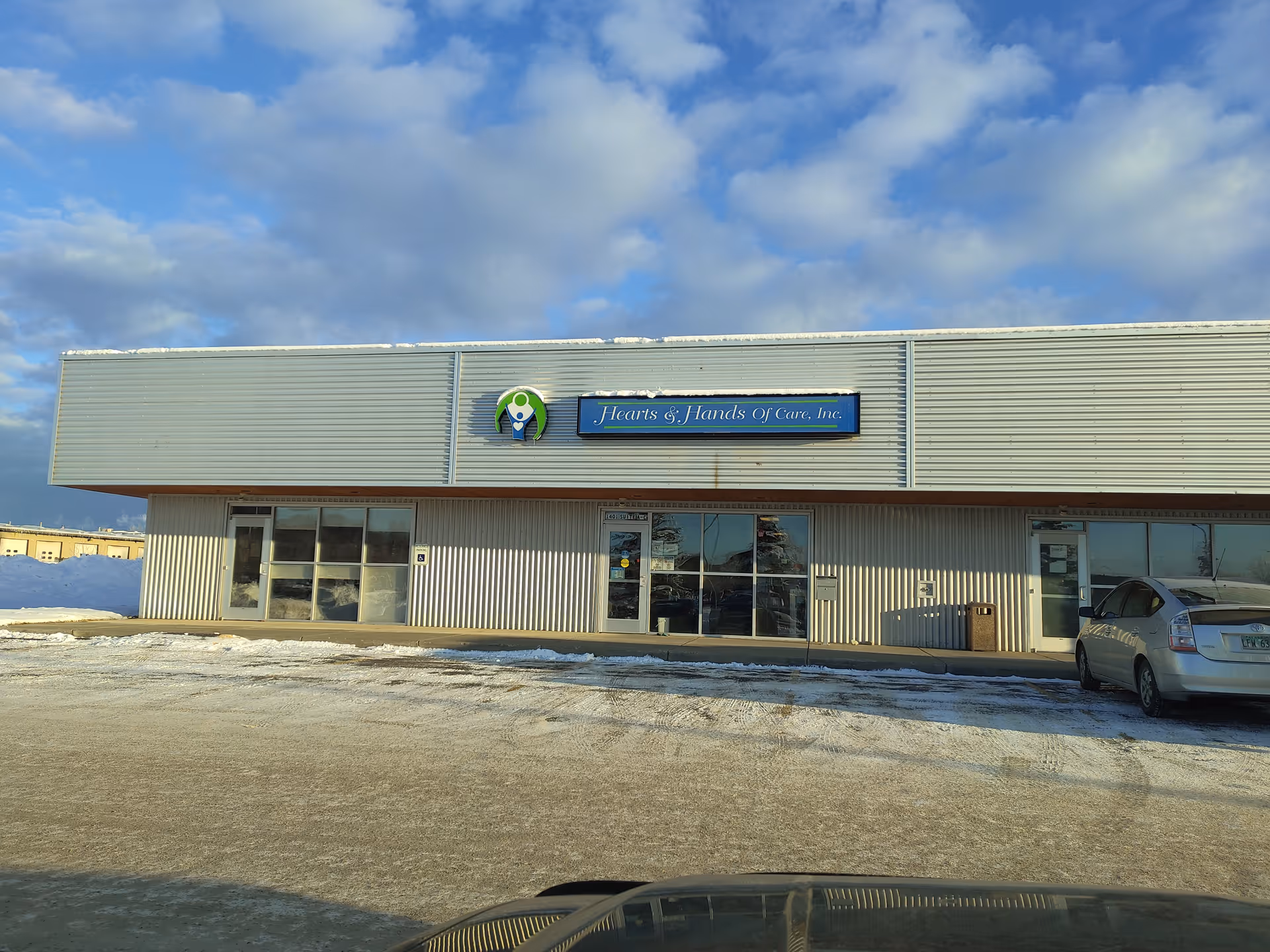 Exterior view of Heart and Hands of Care building with sign and parked car.