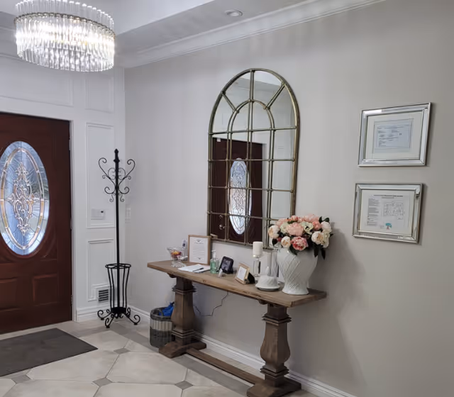 Elegant entryway with chandelier, large mirror, console table, and flowers.