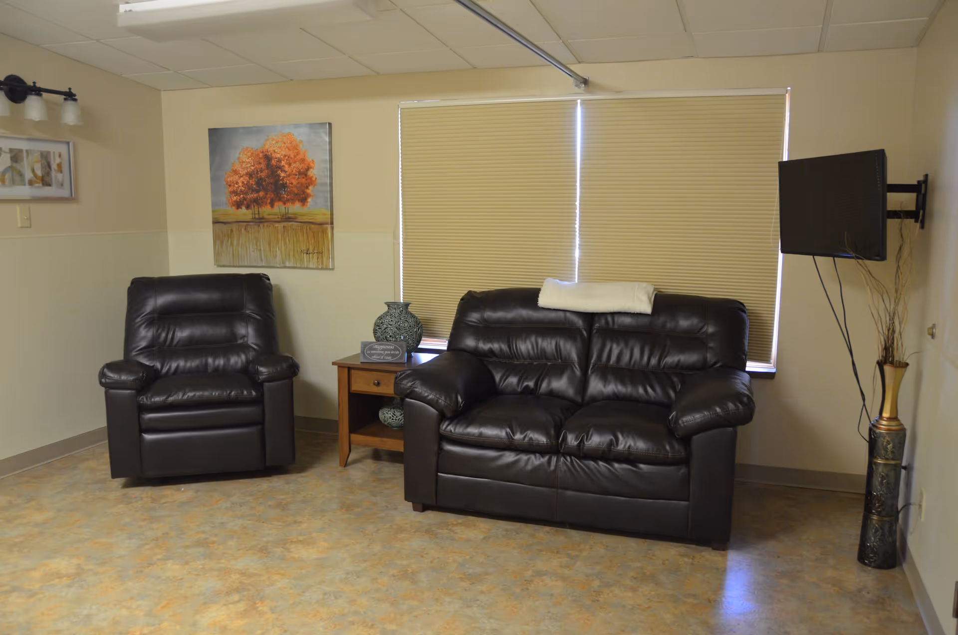 Cozy living room area with black leather sofa, armchair, and wall-mounted TV.