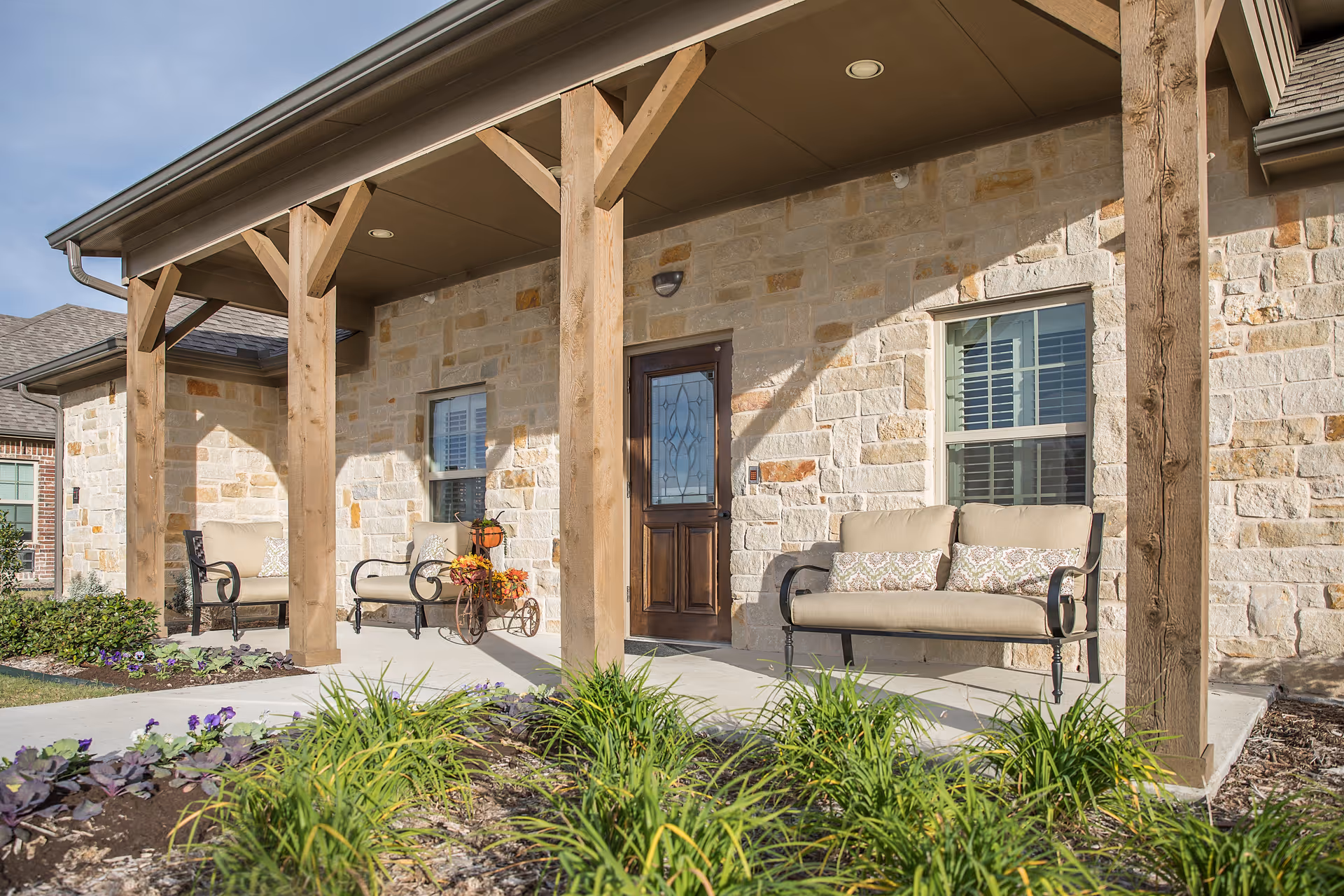 Stone exterior with a covered porch, wooden posts, and cushioned seating at the front entrance.