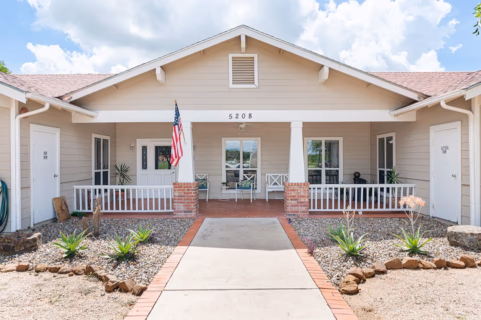 Front view of The Bridges at Edinburg Assisted Living entrance with porch and flag.