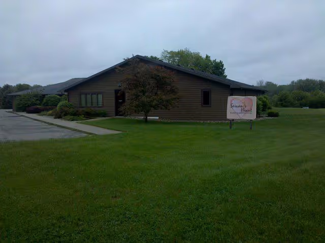 A single-story brown building with a sign on a grassy lawn and parking lot.