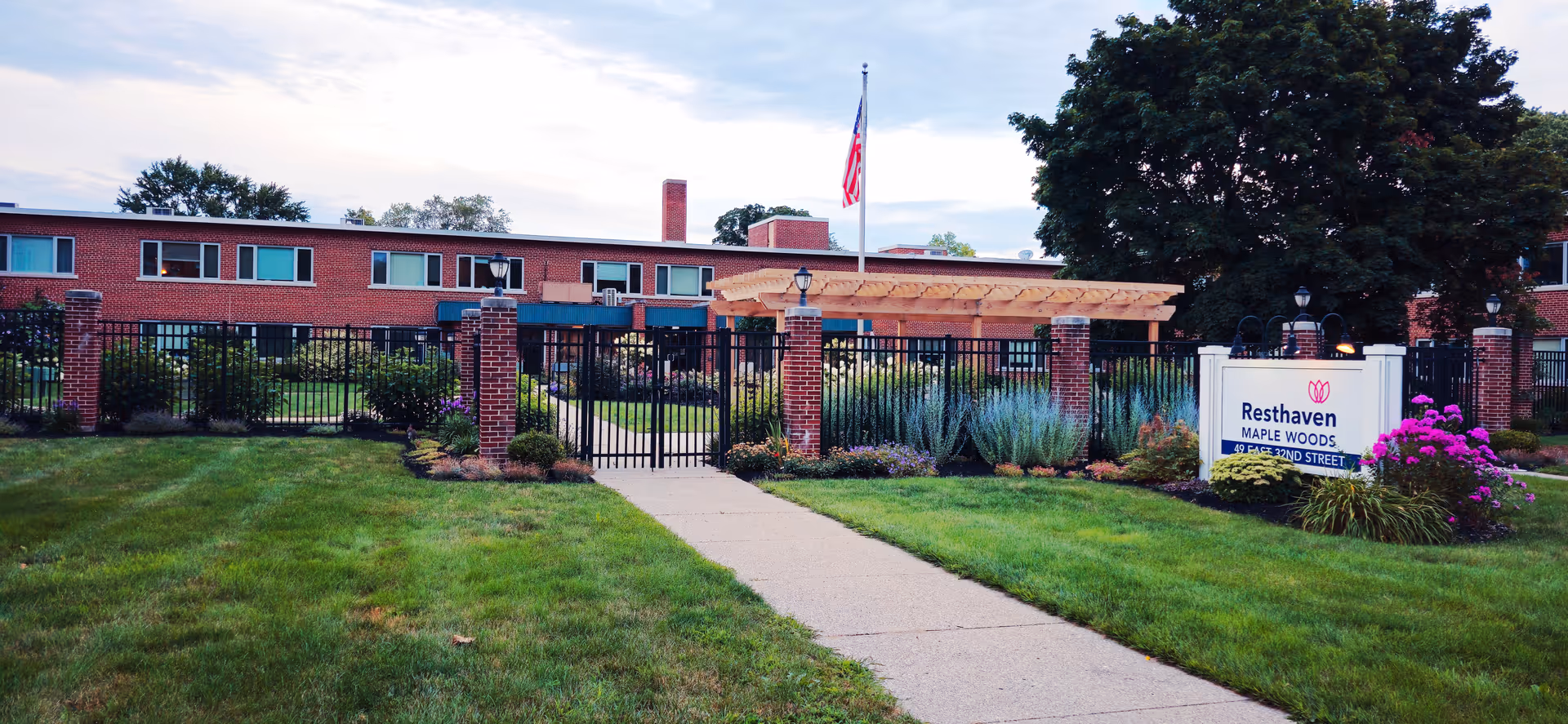 Brick senior living building behind a black fence, landscaped front yard, and Resthaven Maple Woods sign.
