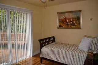 A small bedroom features a striped bed, painting, and a sliding glass door to a deck.