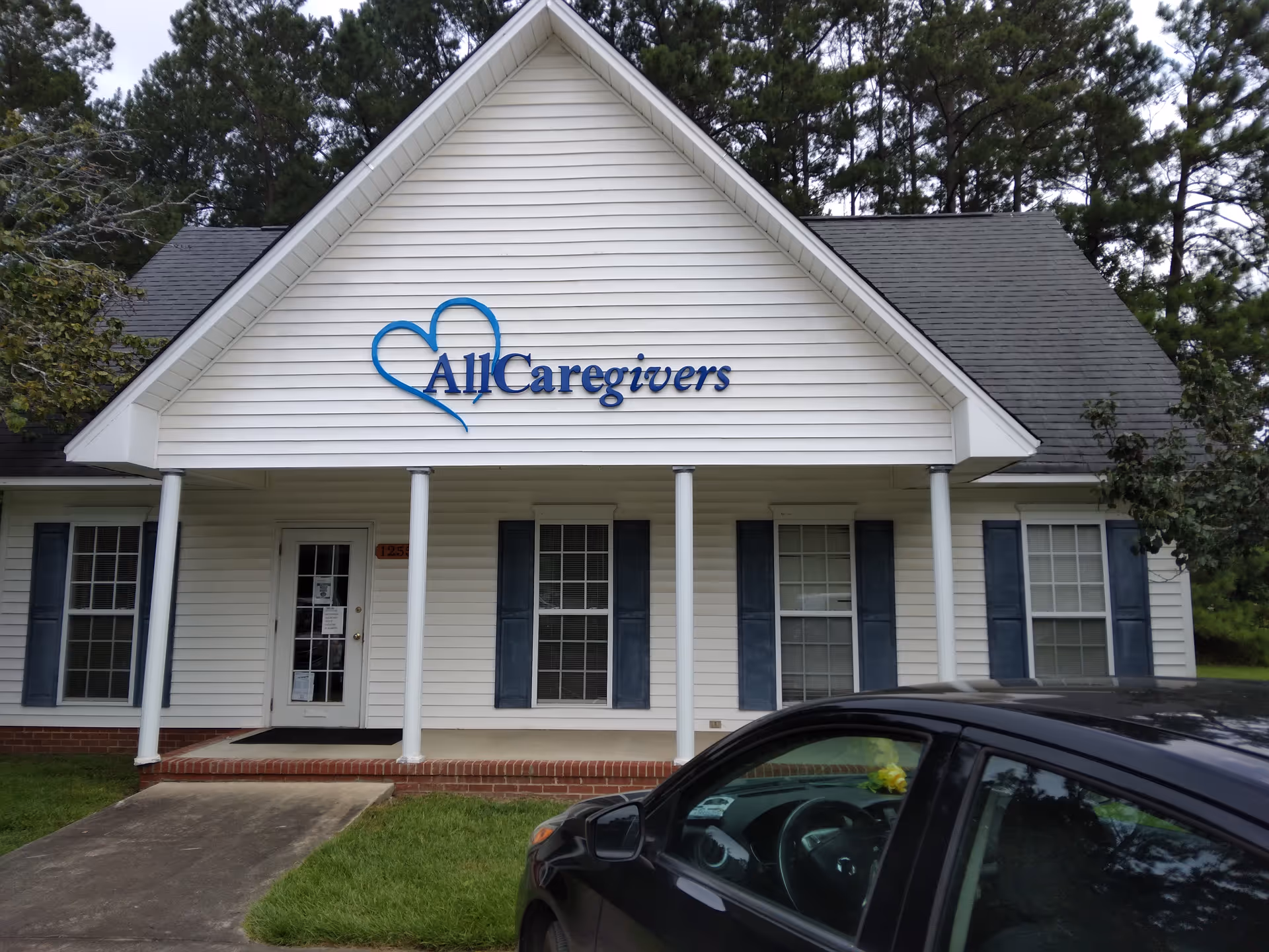 Front exterior of AllCaregivers building with sign, columns, and a parked car.