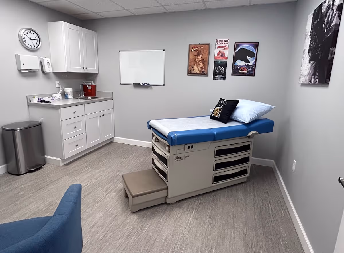 Clinical examination room with an exam table, sink, cabinet, and wall posters.