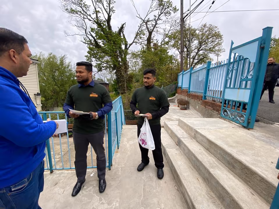 Staff outside Jamaica Social Adult Day Care discuss papers by blue railing near steps.