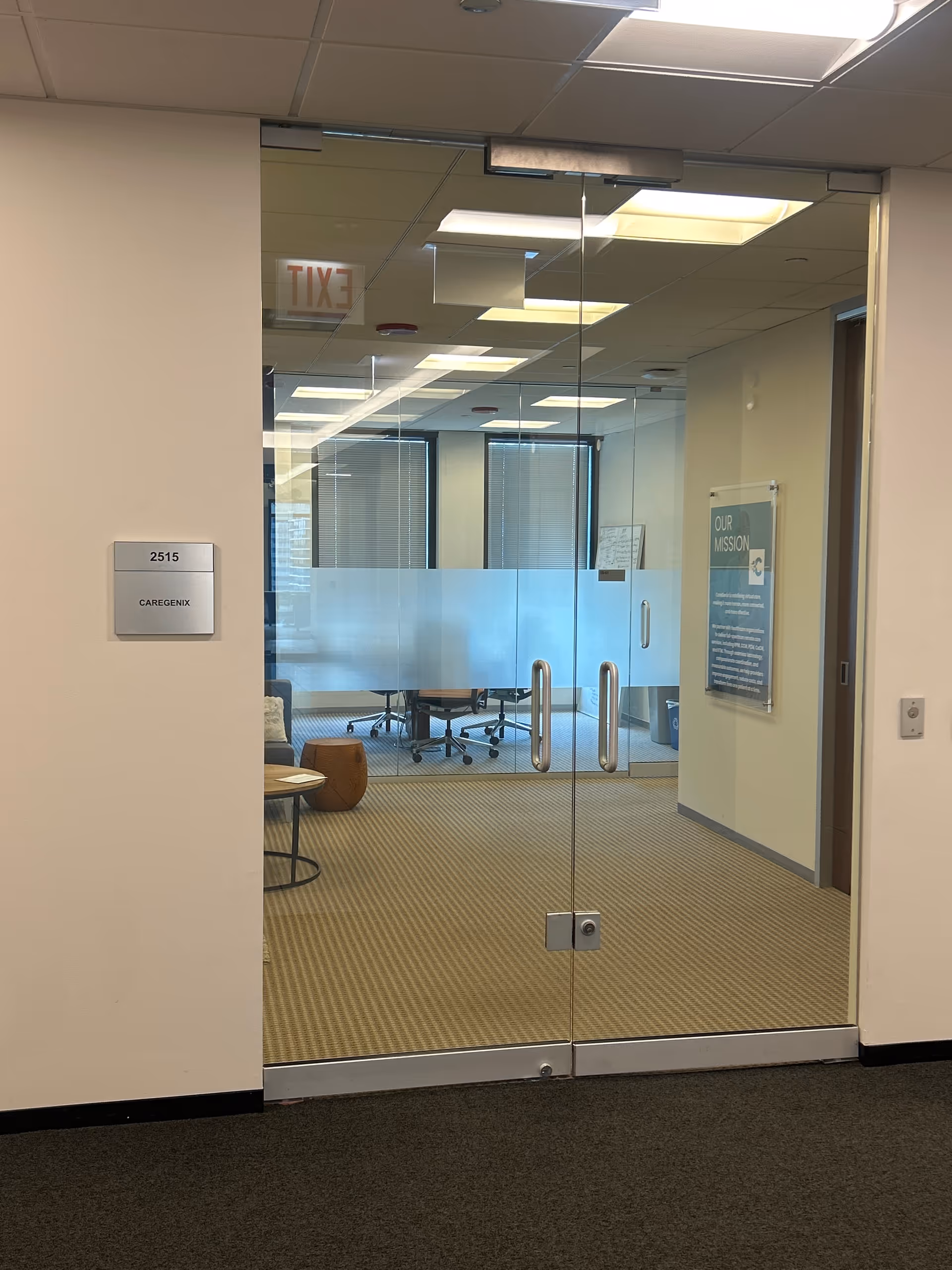 Glass door opening to a meeting room with chairs, tables, and frosted panels.