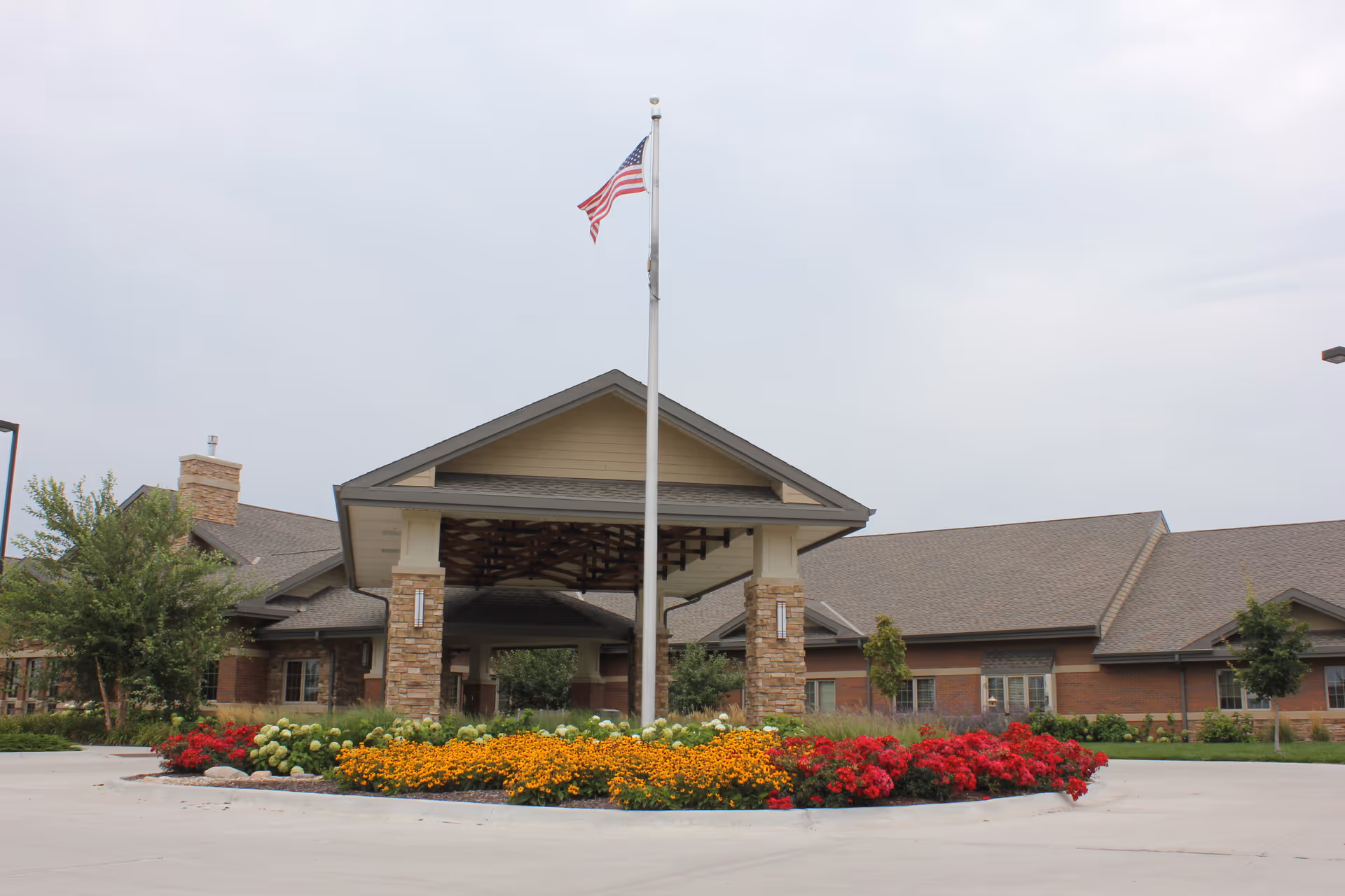 Front view of Willow Brook Assisted Living with flagpole and colorful flower bed.