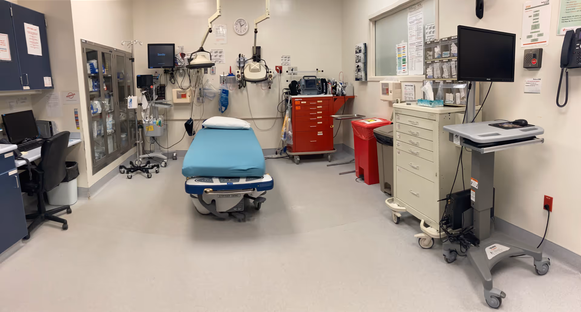 A hospital procedure room with a blue patient bed and extensive medical equipment.
