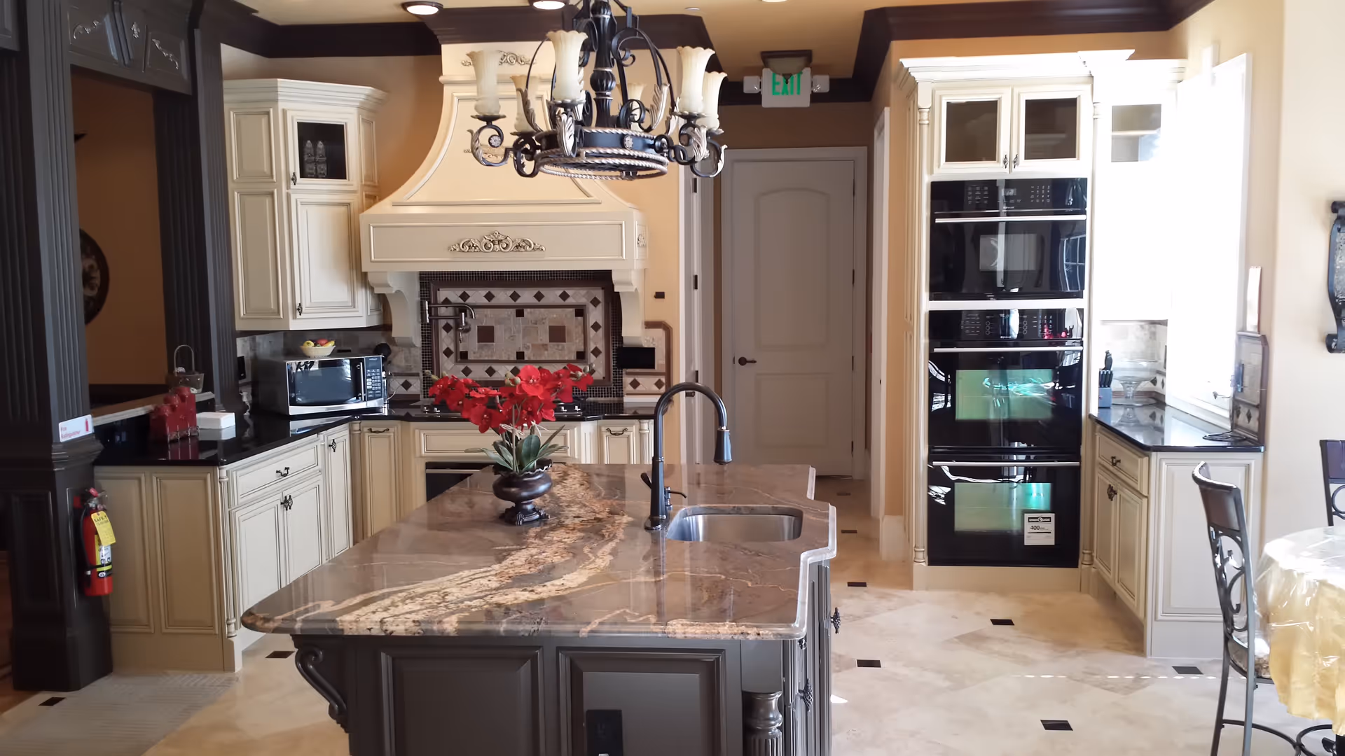Spacious upscale kitchen with a marble island, chandelier, cream cabinetry, and built-in ovens.