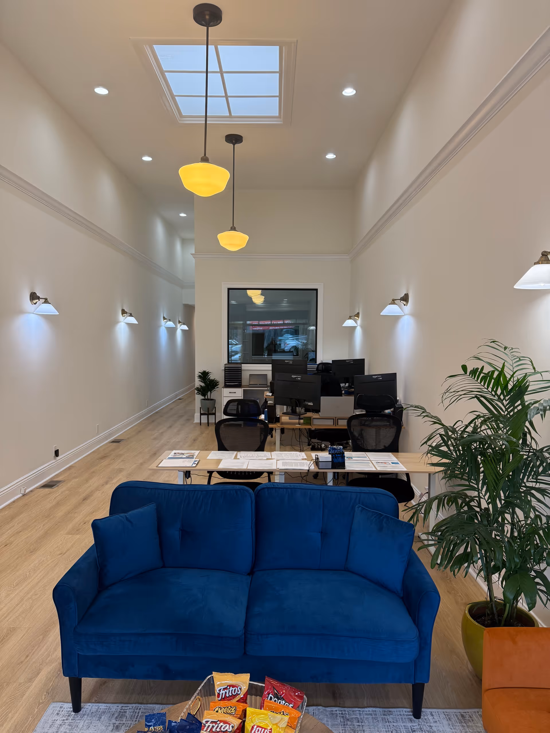 Bright reception area with blue sofa, computers, desks, plants, and snacks in a spacious facility lobby.