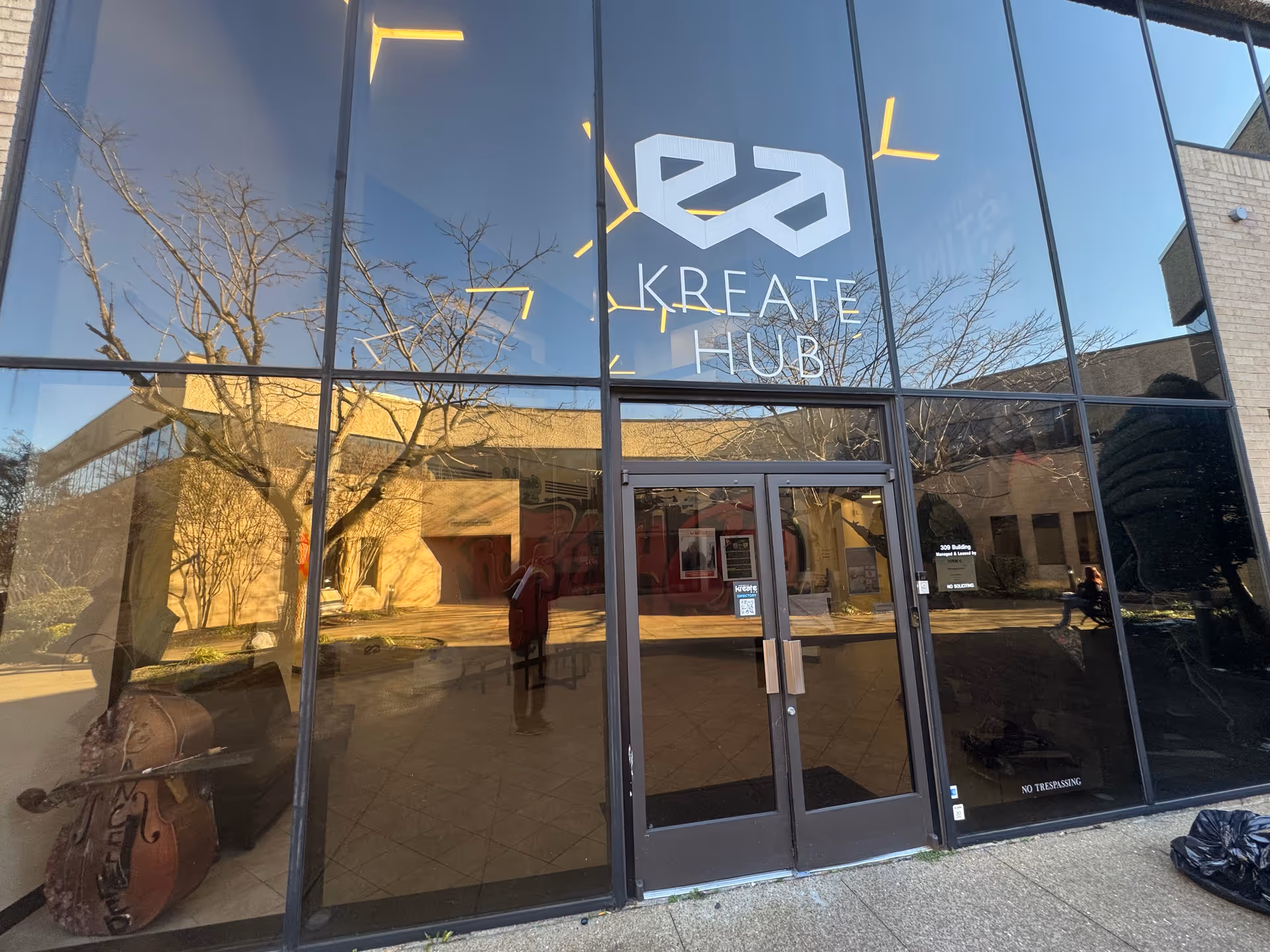 Glass storefront entrance with reflections of trees and the Create Hub sign.