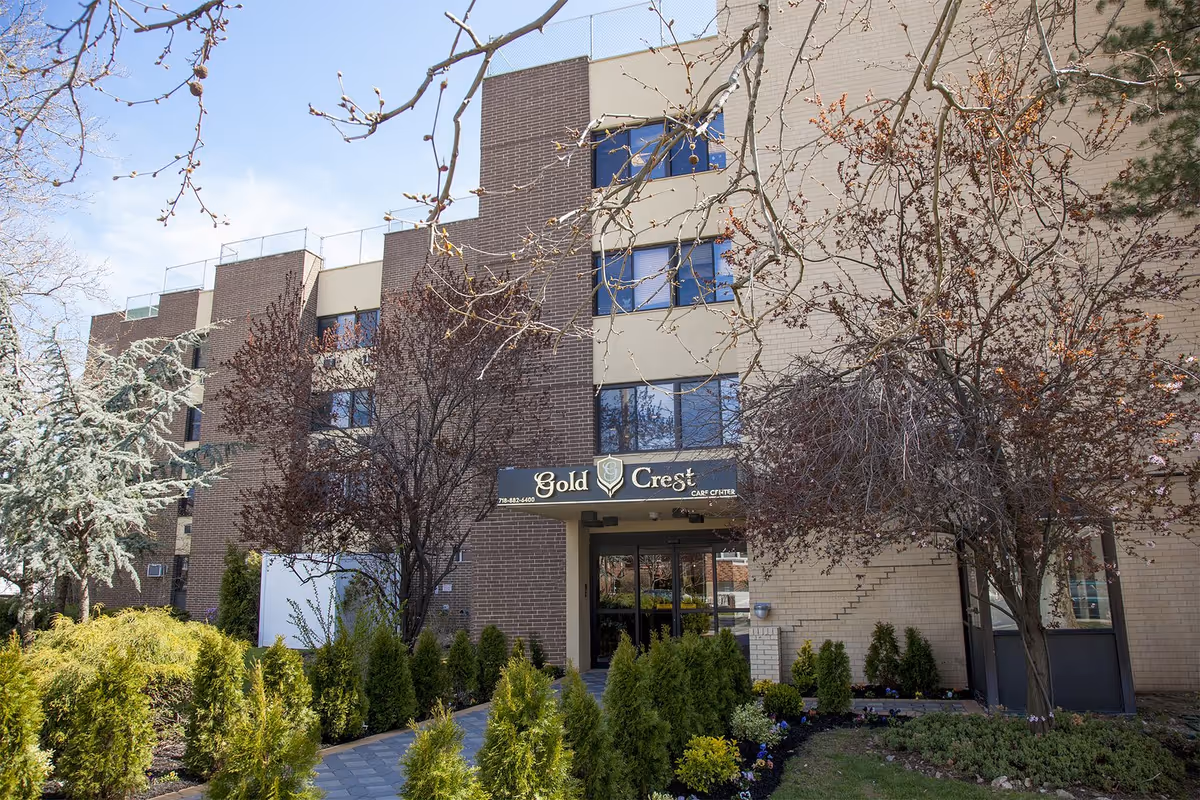 Exterior view of Gold Crest Care Center entrance with trees and shrubs.